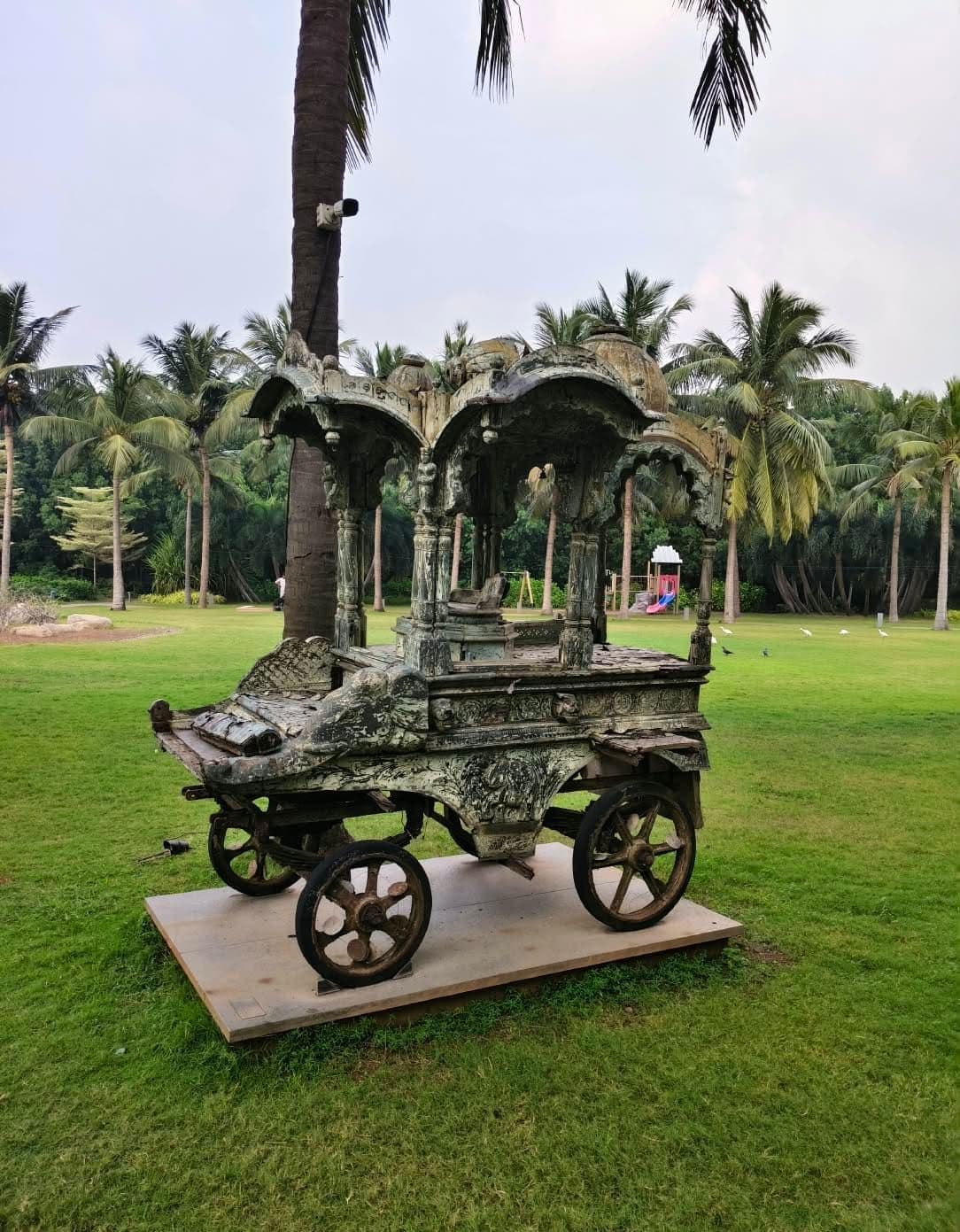 A restored antique wooden bullock cart displayed on a palm-shaded resort lawn