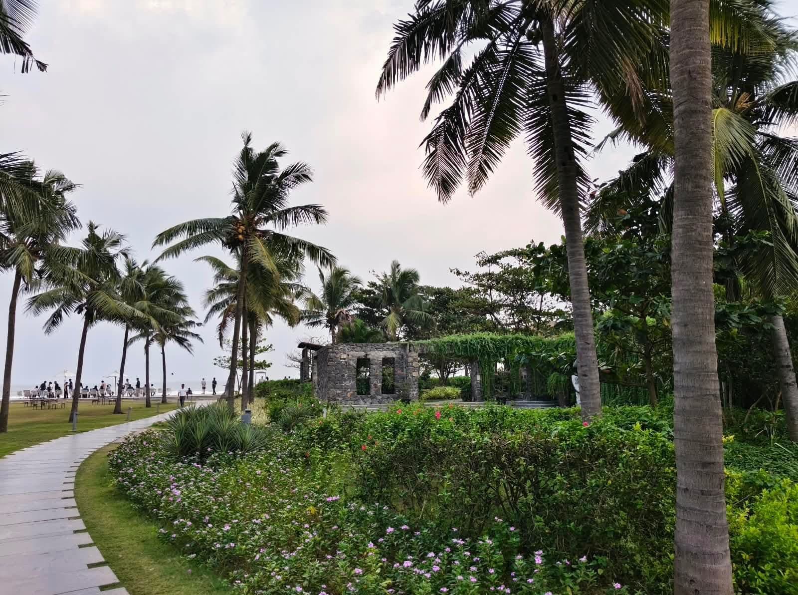 A stone ruin-style garden folly surrounded by palms and flowering shrubs at a coastal resort