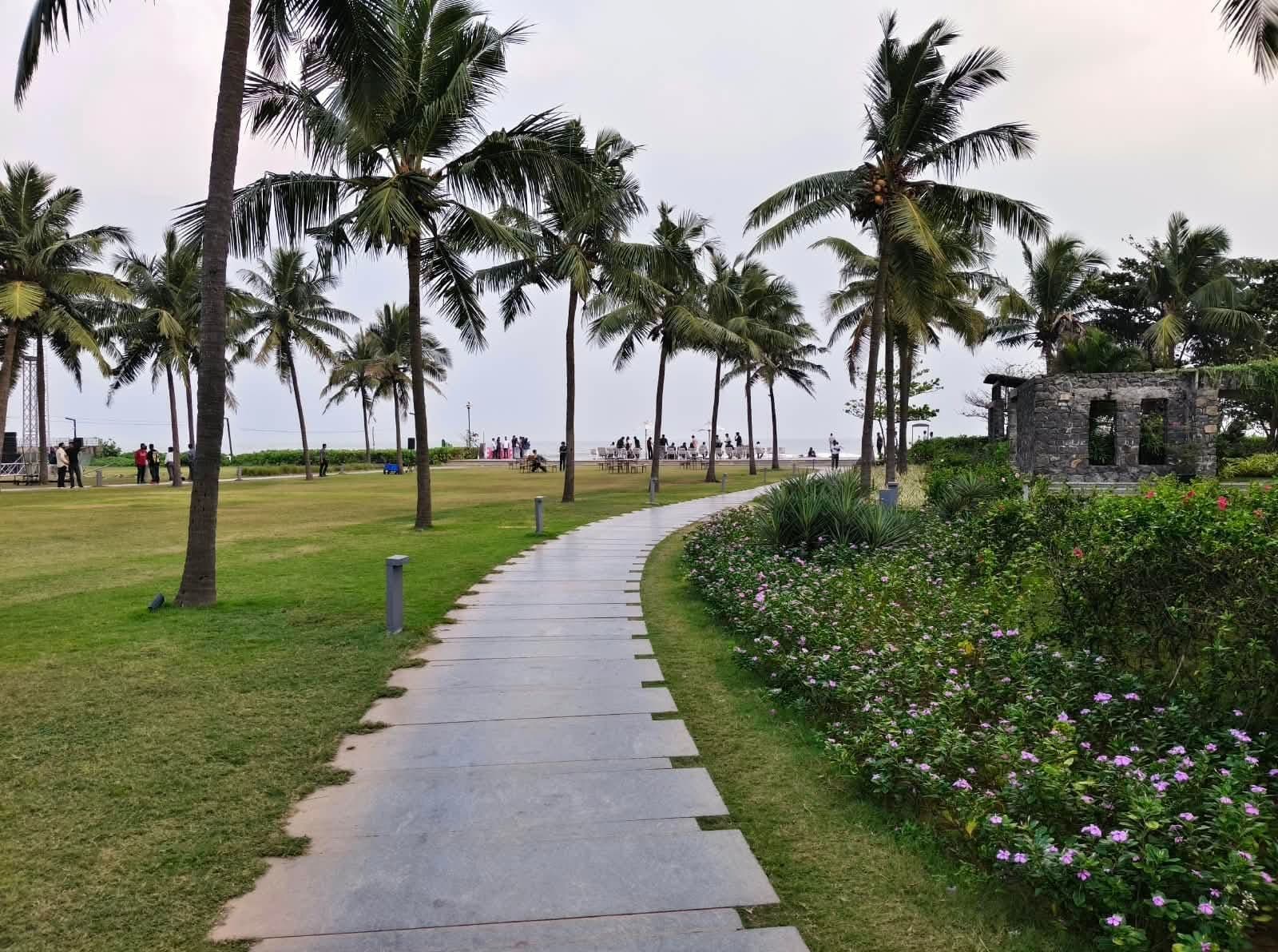 A stone walkway lined with palm trees leading towards the beach at a coastal resort